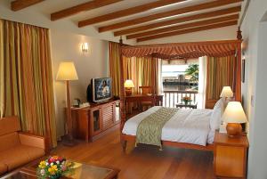 a bedroom with a bed and a television and a couch at Lemon Tree Vembanad Lake Resort, Kerala in Alleppey