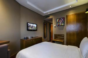 um quarto com uma cama branca e uma televisão na parede em Belere Hotel Rabat em Rabat