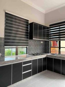 a kitchen with black cabinets and a large window at afza Homestay Paka A in Paka