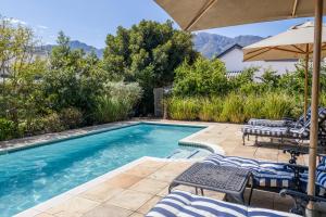 a swimming pool with chairs and an umbrella at Petit Ermitage in Franschhoek