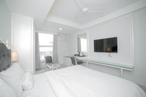 a white bedroom with a bed and a desk with a tv at Pearl Courtyard in Varanasi