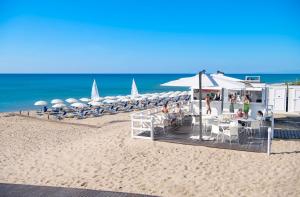 una playa con un grupo de sombrillas, mesas y sillas en Ethra Reserve Calanè en Castellaneta Marina 