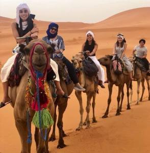 een groep mensen die kamelen berijden in de woestijn bij Hotel Riad Le Petit Prince in Merzouga