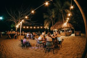 Viajero Tayrona Hostel & Ecohabs في بوريتاكا: مجموعة من الناس يجلسون على الطاولات على الشاطئ في الليل