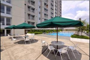 eine Terrasse mit Tischen, Stühlen, Sonnenschirmen und einem Pool in der Unterkunft Cozy corner in South Jakarta in Jakarta