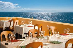 a restaurant with white tables and chairs and the ocean at Sunshine Corfu Hotel And Spa in Nisaki