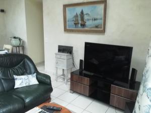 sala de estar con sofá de cuero negro y TV de pantalla plana en La maison au bord de l'eau, en Plouigneau