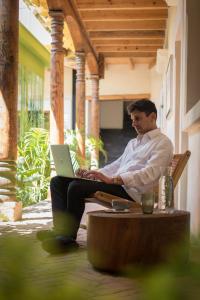 a man sitting in a chair with a laptop on his lap at Taller de Juan - Casa Hotel in San Cristóbal de Las Casas