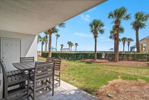 eine Terrasse mit einem Tisch, Stühlen und Palmen in der Unterkunft Bristol 109 - Lovely Ground Floor Beachfront Unit in Gulf Shores