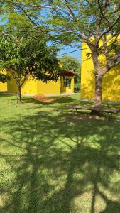 a yellow building with trees and a bench in the grass at Pousada Chalés Praia Vermelha in São João Batista do Glória