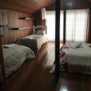 two beds in a room with wooden walls and wood floors at Casarão Villa maggi in Canela