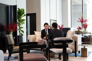 two men talking in a room with chairs and tables at Ascott Thonglor Bangkok - SHA Plus Certified in Bangkok