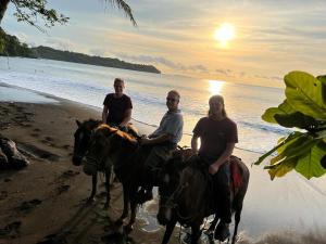 three men riding horses on the beach at sunset at Hotel Gitana Corcovado, y Tour operador in Drake