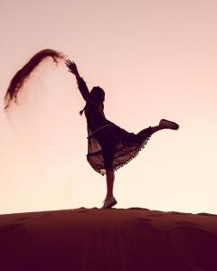 a man is standing on a hill with his leg in the air at Merzouga Premium Desert Camps in Merzouga