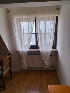 Zimmer mit einem Fenster mit weißen Vorhängen und einem Stuhl in der Unterkunft Dom nad morzem u Ewy Chłopy in Chłopy