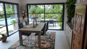 uma sala de jantar com uma mesa e cadeiras de madeira e uma sala de jantar com janelas em Villa d’archi. piscine privée en écrin de verdure em Mérignac