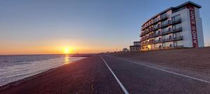 a building on the beach with the sunset in the background at Hotel Lands End in Den Helder