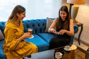 dos mujeres sentadas en una sala mirando sus celulares en Ambassador, a Boutique Hotel en Amán