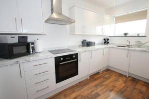 cocina blanca con armarios blancos y fogones horno superior en High Tide apartment with sea views, en Whitley Bay