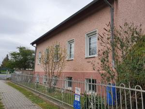 un bâtiment rose avec une clôture devant lui dans l'établissement Gemütliches Souterrain, Schönefels-Free Parking Waßmannsdorf, à Selchow