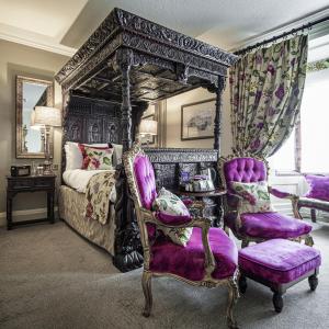 a bedroom with a canopy bed and purple chairs at The Castle Hotel, Conwy, North Wales - The Coaching Inn Group in Conwy