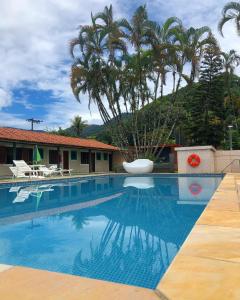 a swimming pool with a palm tree and a building at Hotel Pousada Nosso Cantinho in Ubatuba