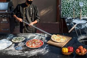 a man is holding a large pizza on a table at Saffronstays Casa Del Palms, Alibaug - luxury pool villa with chic interiors, alfresco dining and island bar in Alibaug