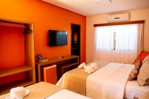 a hotel room with two beds and a television at Pousada das Flores in Coqueiro