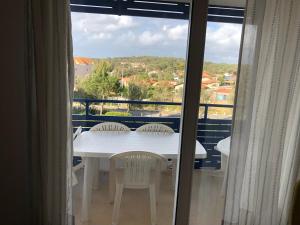 d'une table et de chaises blanches sur un balcon avec fenêtre. dans l'établissement Appartement Climatisé avec Piscine & Mer Bleu Marine, à Lacanau-Océan