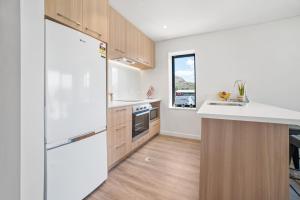 a kitchen with a white refrigerator and wooden cabinets at Toru Top Floor Apartment - Brand New & Convenient in Queenstown