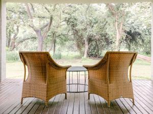 - 2 chaises en osier et une table sur une terrasse couverte dans l'établissement Lilayi Lodge, à Lusaka