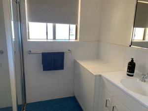 uma casa de banho branca com um chuveiro e um lavatório. em Sunny, 2-bedroom apartment with pool, 200m from Caseys beach em Batehaven