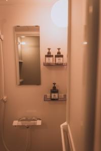 Baño con espejo y 2 botellas en la pared en ゲストハウスまたたび en Matsumoto