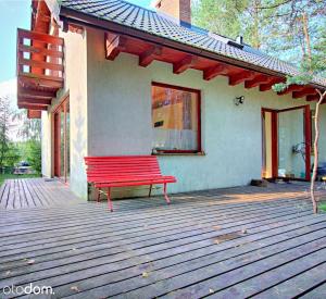 un banco rojo sentado en el porche de una casa en Dom całoroczny w Borach Tucholskich, en Klocek