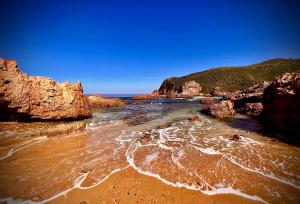 a beach with rocks and the ocean on a clear day at Stay @ 24 Malachite in Knysna