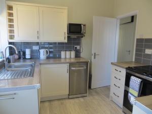 uma cozinha com armários brancos, um lavatório e um fogão em Honeystones em Hunstanton