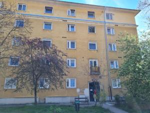 a large yellow building with white windows and a tree at Tatabánya Újvárosi lakás in Tatabánya