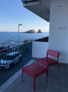 2 rote Stühle auf einem Balkon mit Meerblick in der Unterkunft APPARTAMENTO FRONTE MARE ACi TREZZA in Aci Castello