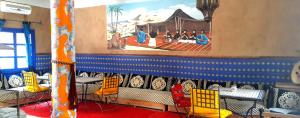 un restaurante con sillas amarillas y una pintura en la pared en Relais Hamada Du Draa, en Mhamid