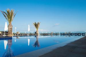a swimming pool with palm trees and the ocean at Hotel Club Sunway Punta Prima in Es Pujols