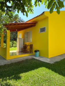 a yellow house with a table and a refrigerator at Pousada Chalés Praia Vermelha in São João Batista do Glória