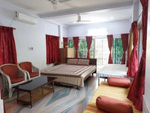 a room with two beds and chairs and red curtains at Chaiti Eco Homestay- Santiniketan Bolpur in Bolpur