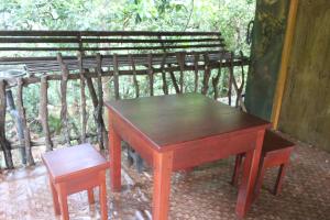 un tavolo di legno e uno sgabello accanto a una panchina di sinharaja Aranuwa resort a Nelluwa