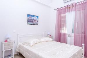 a white bedroom with a white bed and pink curtains at Eliora Studio & Aelia Apartment in Heraklio
