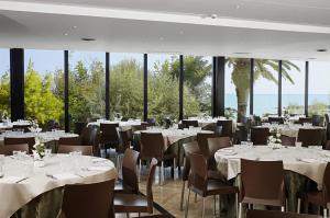 um restaurante com mesas e cadeiras brancas e janelas em Serena Majestic Hotel em Montesilvano