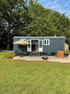 a green tiny house with a patio and a grill at The Bibury - Westwell Downs Shepherd Huts in Oxford