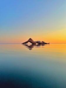 Eine Frau, die bei Sonnenuntergang im Wasser liegt. in der Unterkunft Vivid Blue Serenity Resort in Sveti Stefan