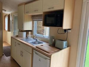 a small kitchen with a sink and a microwave at Cosy Quiet Static Caravan Mawgan Porth St Eval in Wadebridge
