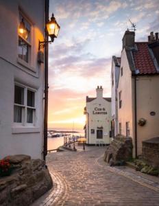 a street with buildings and a sunset in the background at The Anchorage your home in idyllic Staithes in Staithes