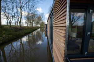 una casa flotante en un río con la puerta abierta en Waterlodges WeidumerHout, en Weidum